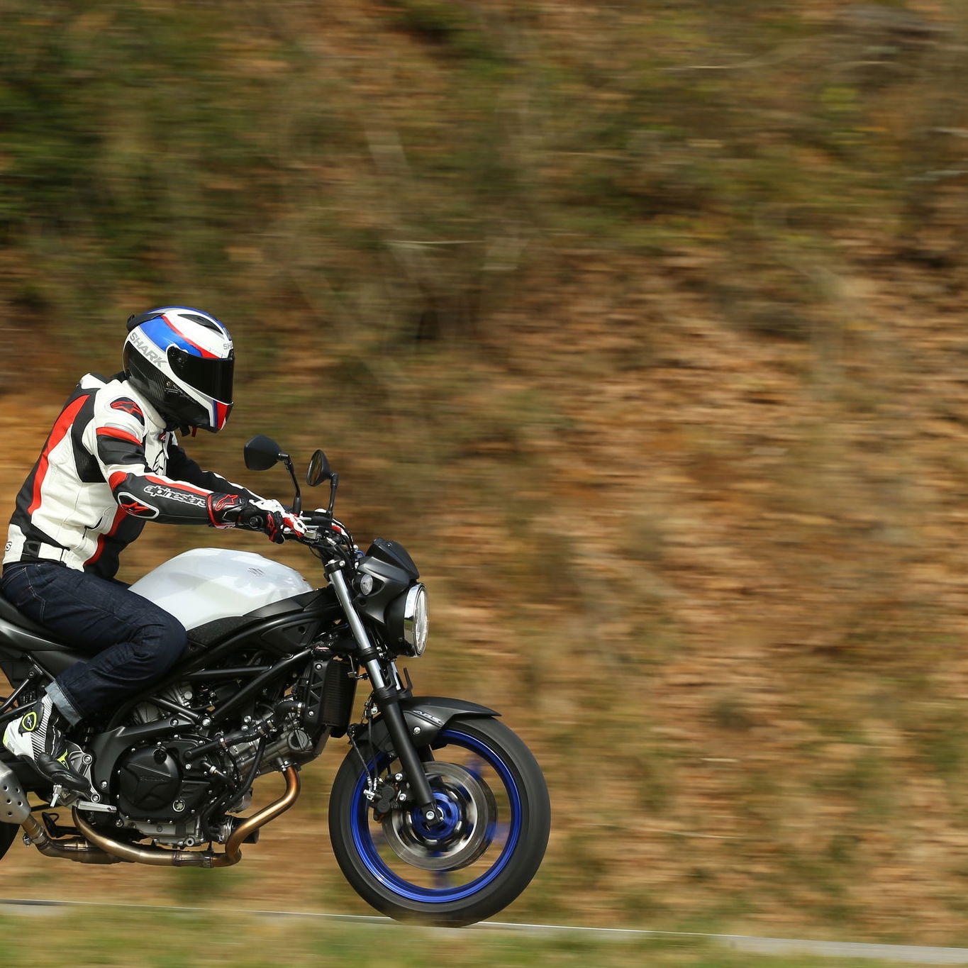 A black and white 2016 Suzuki SV650 motorbike being ridden down a country road